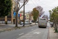 cars, trucks and buses driving along a street with lush green trees and autumn colored trees, apartments and retail stores