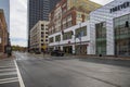 Cars and trucks driving on a street with people walking along the sidewalk with retail stores, apartments and skyscrapers