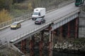 Cars and trucks pass over an old and rusty metallic bridge