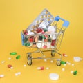 cart full of pills and vitamins on bright yellow background.