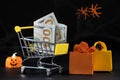 Cart with money hundred-dollar bills, paper bags for purchases. Halloween Sale Royalty Free Stock Photo