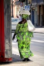 Cartagena, Murcia, Spain - August 01 2018: An Afro-Caribbean woman in bright green traditional african clothing, carrying goods on