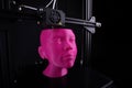 A cartesian 3D-printer manufactures a humanoid head from bright pink plastic. Royalty Free Stock Photo