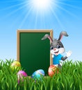 Cartoon bunny waving hand with easter eggs and green chalkboard in the grass Royalty Free Stock Photo