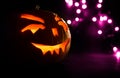 Carved face of pumpkin glowing on Halloween on purple bokeh light background