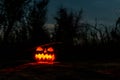Carved halloween pumpkin jack-o-lantern wearing witch hat with burning candles glows in a darkness. Spooky landscape Royalty Free Stock Photo