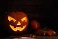 Carved halloween pumpkin with a scary glowing face on dark rustic wood as an autumn decoration, copy space