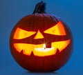 Carved pumpkin for Halloween jack-o\'-lanterns with scary smiles and burning candle inside isolated on blue background Royalty Free Stock Photo