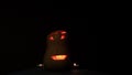 A carved pumpkin lantern burning in the dark and candles for Halloween.