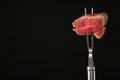 Carving fork with pieces of steak and space for text on black background.