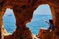 Girl sitting in a cave hole and pointing on a boat at Algar Seco