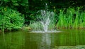 Cascade fountain on emerald surface of old pond against background of greenery of shady garden. Royalty Free Stock Photo