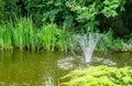 Cascade fountain on emerald surface of pond in the old shady garden. Freshness and coolness Royalty Free Stock Photo