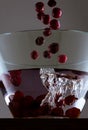 Cascade of red cherries falling into a bowl of water on a wooden surface Royalty Free Stock Photo