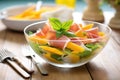 cascading melon and prosciutto salad with basil leaves in a glass bowl