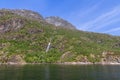 A cascading waterfall tumbles down a rocky mountainside into a fjord in Trollfjorden, Norway