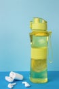 A case with wireless headphones and a sporty yellow water bottle on a blue background Royalty Free Stock Photo