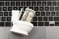 Cash dollars inside in Miniature of toilet bowl on laptop keyboard. Concept of internet fraud or lost money. Financial