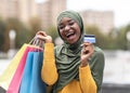 Cashback bonus. Happy islamic female holding credit card and shopping bags outdoors Royalty Free Stock Photo