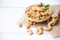 Cashew nuts with green leaves in basket and spoon isolated on white wooden background