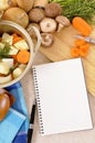 Casserole stockpot with organic vegetables and herbs on kitchen worktop with blank cookbook or recipe book, copy space Royalty Free Stock Photo