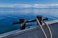 Cast iron, black, with signs of corrosion mooring device with a rope and background of blue Baikal lake in summer