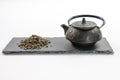 Cast-iron black teapot and handful of leaf green tea on rectangular shale plate Royalty Free Stock Photo