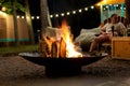 Cast iron fire pit campfire place at forest beach camping with brgiht burning flame at evening time against light bulb Royalty Free Stock Photo