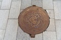 Cast iron manhole cover with embossed maple leaf is positioned on the gray concrete slab sidewalk