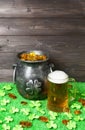 Cast iron pot, decorated by four-petal lucky shamrock leaf, full of leprechaun gold treasure, mug of beer, clover leaves and gold Royalty Free Stock Photo