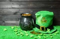 Cast iron pot with treasure and leprehaun hat, clover leaves and coins on green grass, dark wooden planks background. Saint Royalty Free Stock Photo