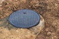 A cast-iron sewer manhole surrounded by a puddle of water at a construction site. Construction of sewer wells Royalty Free Stock Photo