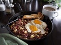 Corned beef hash with sunnyside up eggs in cast iron skillet.