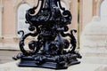 cast iron, wrought iron and forged steel decorative, ornate shiny black lamppost detail. soft blurred stone building elevation Royalty Free Stock Photo