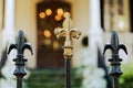 A cast wrought iron fence lined with black and gold fleur de lis post toppers with a New Orleans southern style home in Royalty Free Stock Photo