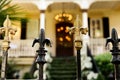 A cast wrought iron fence lined with black and gold fleur de lis post toppers with a New Orleans southern style home in