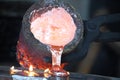 Casting liquid red hot metal from crucible held with tongs