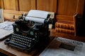 Castle interior, wooden writing desk, table near windows, black vintage antique typewriter, blank sheet of paper inserted,