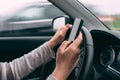 Casual adult caucasian woman typing text message on mobile smart phone while driving her car on overcast autumn day, selective Royalty Free Stock Photo