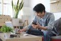 Casual asian man using mobile phone while working online at home with computer laptop Royalty Free Stock Photo