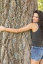 Casual attractive brunette embracing a tree looking at camera