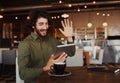 Casual bearded man waving his hand while talking through video-chat in smartphone while relaxing in cafe Royalty Free Stock Photo