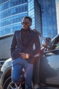 Casual black man in sunglasses posing near car in town.