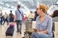 Woman using her cell phone while waiting to board a plane at departure gates at international airport.