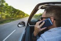 Casual businessman talking on cellphone while driving car, side view. Handsome young man in shirt talking on mobile phone while Royalty Free Stock Photo
