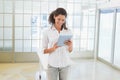 Woman in white shirt and gray jeans holding tablet and smiling while standing in modern office Royalty Free Stock Photo