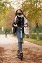 Casual caucasian teenager wearing protective face mask riding urban electric scooter in city park during covid pandemic