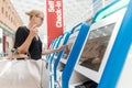 Casual caucasian woman using smart phone application and check-in machine at the airport getting the boarding pass.