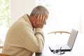 Casual dressed man sitting by a laptop computer is hiding his head in despair. A pair of glasses lying on a pile of papers next to