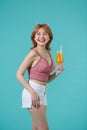 Casual dressed woman holding orange juice with glass, isolated portrait smiling girl on turquoise background Royalty Free Stock Photo